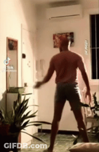 A Man In Shorts Is Dancing In A Room With Plants And A Mirror . GIF