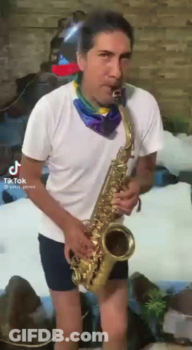A Man In Shorts Is Playing A Saxophone In Front Of A Waterfall . GIF
