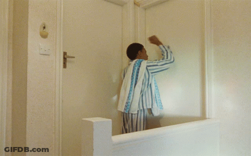 A Man In Striped Pajamas Stands In Front Of A White Door GIF