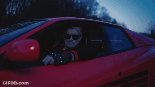 A Man In Sunglasses Is Driving A Red Car GIF