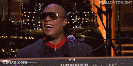 A Man In Sunglasses Is Singing Into A Microphone While Playing A Keyboard . GIF
