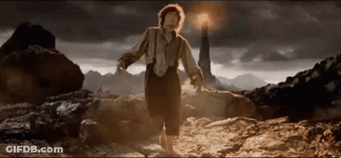 A Man In Suspenders Is Standing In Front Of A Lighthouse In The Desert . GIF