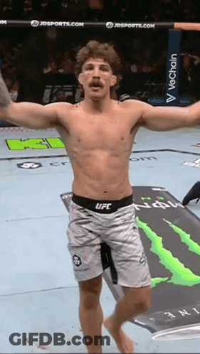 A Man In UFC Shorts Is Standing On A Mat With A Monster Energy Logo In The Background GIF