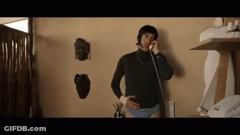 A Man In Underwear Is Talking On A Phone While Standing In A Room . GIF
