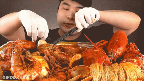 A Man In White Gloves Is Eating A Tray Of Seafood GIF