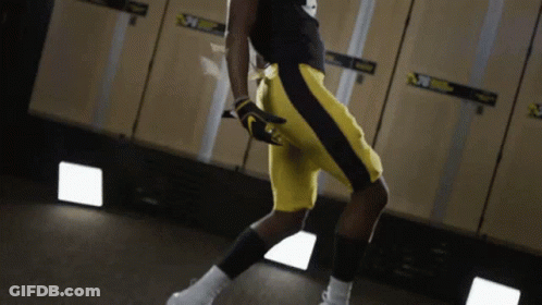 A Man In Yellow Shorts Is Standing In A Locker Room With A Sign That Says ' Nebraska ' On It GIF
