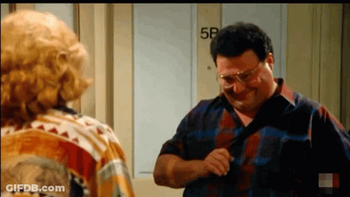 A Man Is Adjusting His Tie While Standing Next To A Woman In Front Of A Door That Says 5B . GIF