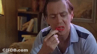 A Man Is Applying Lipstick To His Lips In A Living Room . GIF