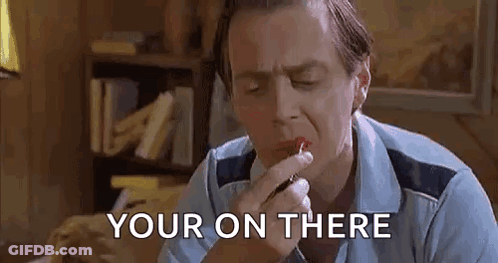 A Man Is Applying Lipstick To His Lips While Sitting At A Table . GIF