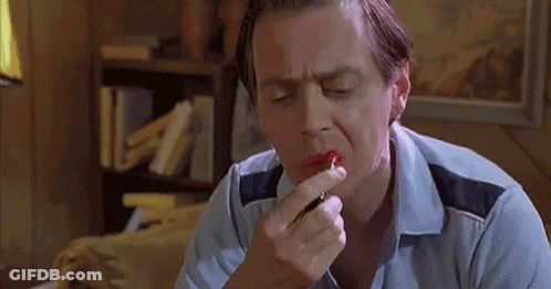 A Man Is Applying Red Lipstick To His Lips In A Room . GIF