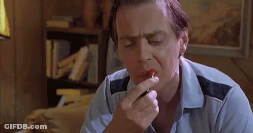 A Man Is Applying Red Lipstick To His Lips While Sitting On A Couch . GIF
