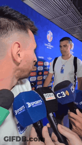 A Man Is Being Interviewed By Several Microphones Including A Sports One GIF