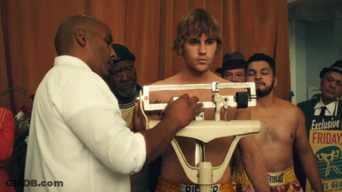 A Man Is Being Weighed On A Scale With A Sign In The Background That Says Exclusive Friday GIF