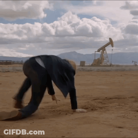 A Man Is Bending Over In The Dirt In Front Of A Oil Pump GIF