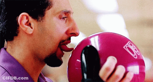 A Man Is Biting Into A Pink Bowling Ball . GIF