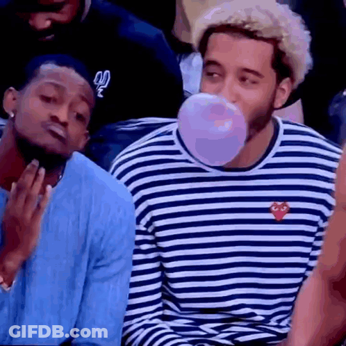 A Man Is Blowing A Bubble Gum While Sitting Next To Another Man In A Striped Shirt . GIF