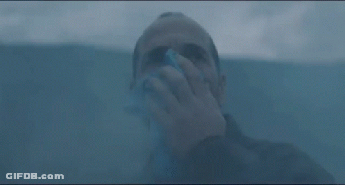 A Man Is Blowing His Nose With A Napkin While Standing In A Dark Room . GIF