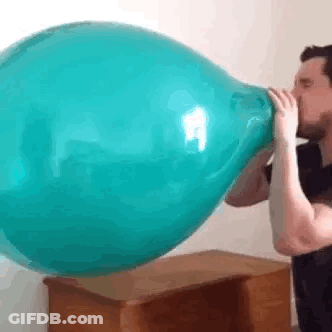 A Man Is Blowing Up A Blue Balloon On A Table . GIF