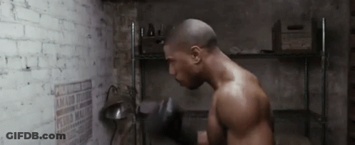 A Man Is Boxing In A Room With A Brick Wall And A Shelf . GIF
