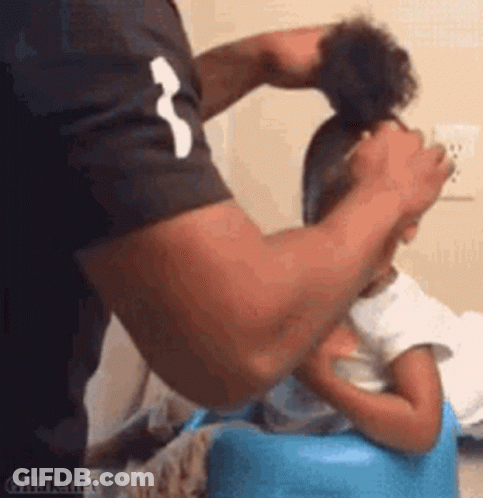 A Man Is Brushing A Little Girl 'S Hair While She Is Sitting On A Blue Chair . GIF