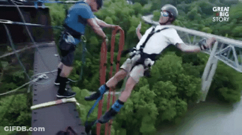 A Man Is Bungee Jumping Off A Bridge While Another Man Helps Him . GIF