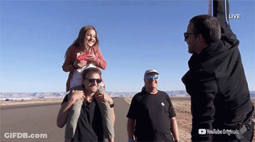 A Man Is Carrying A Girl On His Shoulders While Another Man Watches GIF