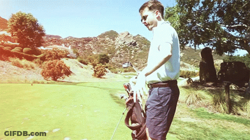 A Man Is Carrying A Golf Bag And A Golf Club On A Golf Course GIF