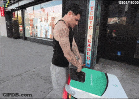 A Man Is Carrying A Green Surfboard In Front Of A Store Called Psychic Reader GIF