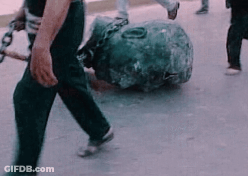A Man Is Carrying A Large Rock With Chains Around It . GIF