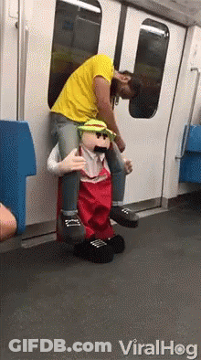 A Man Is Carrying A Puppet On His Shoulders On A Subway Train . GIF