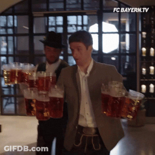 A Man Is Carrying A Stack Of Beer Mugs With The Fc Bayern.tv Logo In The Corner GIF