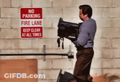 A Man Is Carrying A Suitcase In Front Of A No Parking Fire Lane Sign GIF