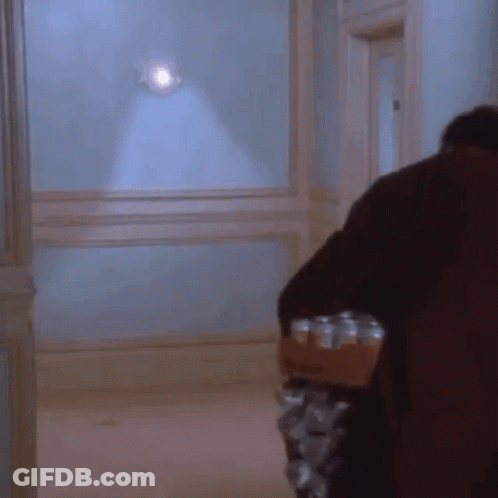 A Man Is Carrying A Tray Of Cans In A Hallway GIF