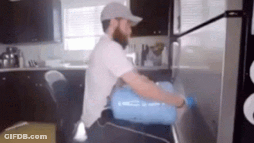 A Man Is Carrying A Water Bottle On His Back Into A Refrigerator . GIF