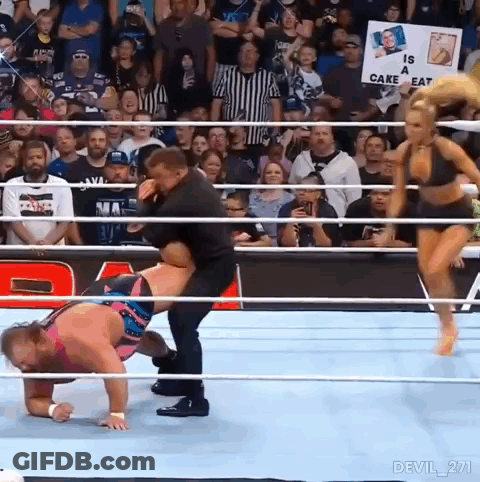 A Man Is Carrying A Woman In A Wrestling Ring With A Sign That Says Is A Cake Eat . GIF