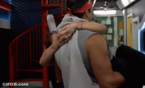 A Man Is Carrying A Woman In His Arms In A Room With A Spiral Staircase GIF