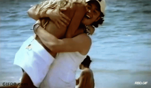 A Man Is Carrying A Woman In His Arms On The Beach With Rbd.gif Written On The Bottom GIF