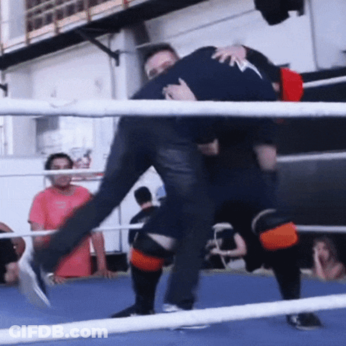 A Man Is Carrying Another Man In A Boxing Ring While Another Man Watches GIF