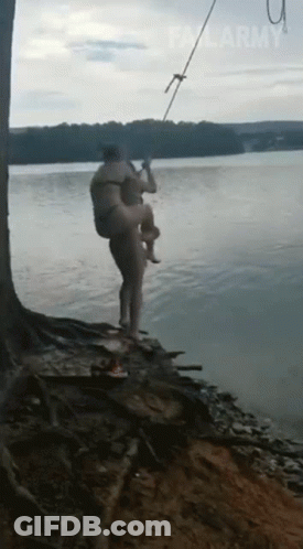 A Man Is Carrying Another Man In His Arms Into The Water . GIF