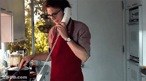 A Man Is Cooking In A Kitchen While Talking On A Phone . GIF