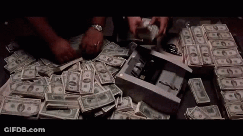 A Man Is Counting Money On A Table With A Bunch Of Money On It . GIF