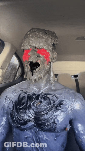 A Man Is Covered In A Thick Gray Substance With Red Paint On His Face GIF