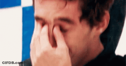 A Man Is Covering His Eyes With His Hand . GIF