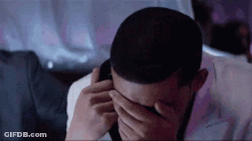 A Man Is Covering His Eyes With His Hands While Talking On A Cell Phone . GIF