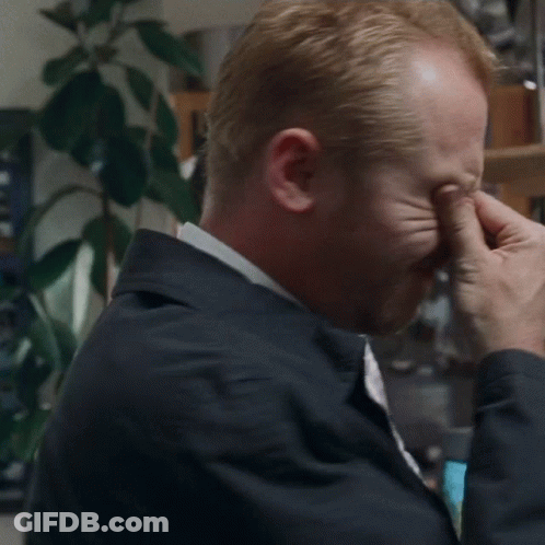 A Man Is Covering His Eyes With His Hands While Wearing A Jacket And Tie . GIF