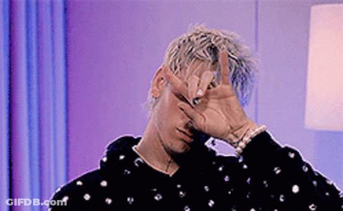 A Man Is Covering His Face With His Hand And Making A Peace Sign . GIF