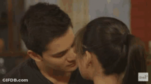 A Man Is Covering His Face With His Hand While A Woman Kisses Him On The Neck . GIF