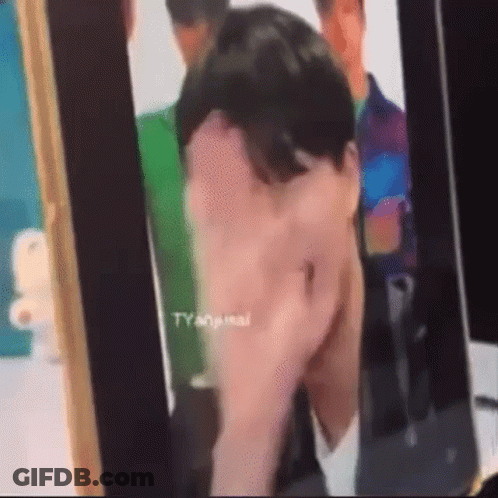 A Man Is Covering His Face With His Hand While Looking At A Picture Of Himself . GIF