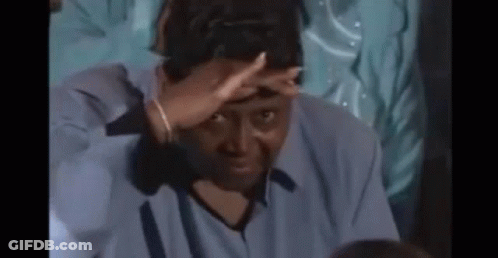 A Man Is Covering His Face With His Hand While Sitting In A Dark Room . GIF