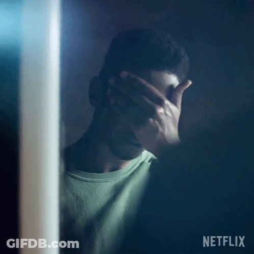 A Man Is Covering His Face With His Hand While Standing In Front Of A Mirror . GIF
